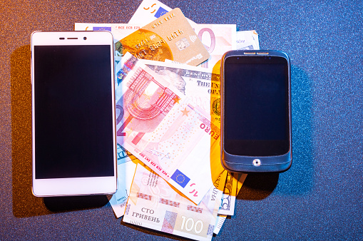 Two smartphones and a variety of currencies. International money transfers. Communication between countries. View from above.