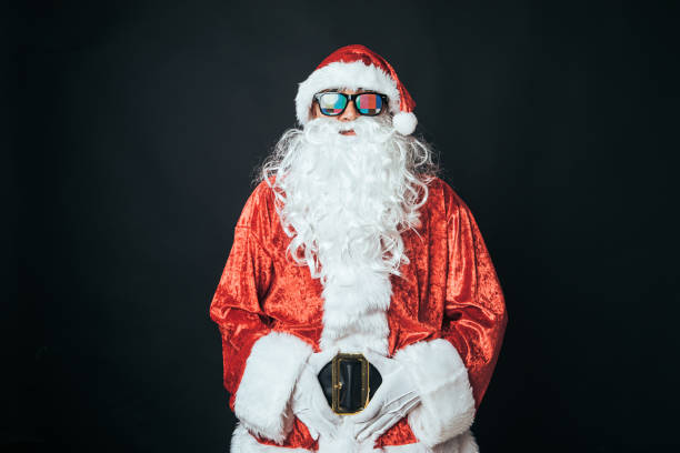 Man dressed as Santa Claus wearing glasses with tv setting letter, on black background. Christmas concept, Santa Claus, gifts, celebration. stock photo