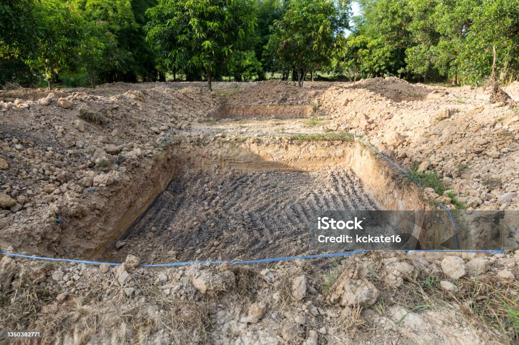 A hole in the ground. Dig the pit for planting saplings. mud hole for planting tree. View of hole in the dirt with preparation for building a pond. Dig rectangle hole on the ground for construction. Abstract Stock Photo