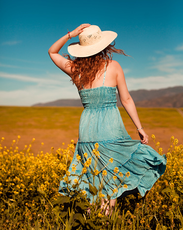 Girl in a yellow flower field spinning holding her hat