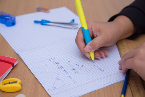 istock Close-up pupil's hand writes a geometric formula in a notebook. 1350385080