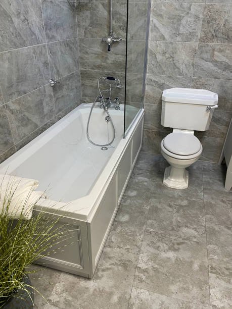 istock Image of luxury bathroom suite with white / grey marble wall tiles, white ceramic bath with chrome Victorian-style mixer tap and shower plumbing, glass shower screen, handle flush WC toilet 1350385275