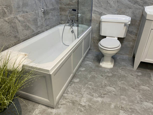 istock Image of luxury bathroom suite with white / grey marble wall tiles, white ceramic bath with chrome Victorian-style mixer tap and shower plumbing, glass shower screen, handle flush WC toilet 1350385301
