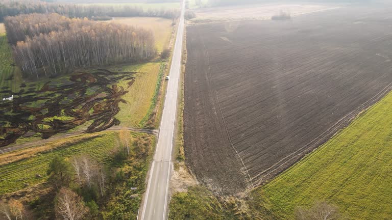 Country narrow road next to arable agricultural fields, aerial view.