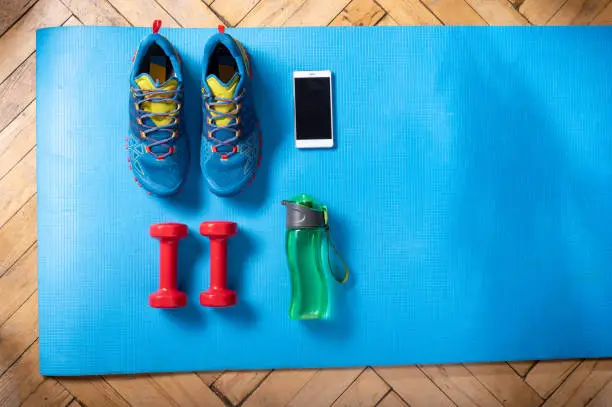 Sports mat. Sports shoes, dumbbells, water and a smartphone. Fitness at home. View from above.