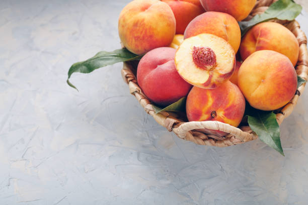 istock Peaches in a wicker basket on a stone gray table with a juicy peach slice with a stone pit. Top view, free space 1350388916