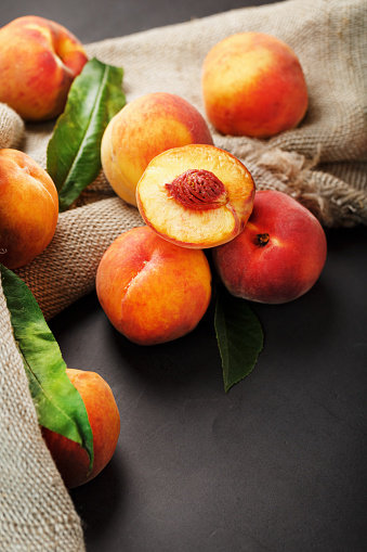 Peach fruit on a black background with a cloth of burlap and green leaves. Sweet and juicy peach slices with a stone