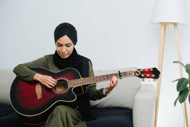 mirando a la mujer musulmana instrumental en la cabeza religiosa tocando la guitarra - headware fotografías e imágenes de stock