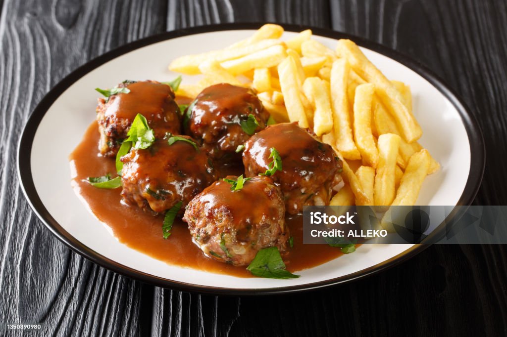 Belgian Boulets sauce lapin meatballs in apple gravy and French fries closeup in the plate. Horizontal Belgian Boulets sauce lapin meatballs in apple gravy and French fries closeup in the plate on the table. Horizontal Meatball Stock Photo