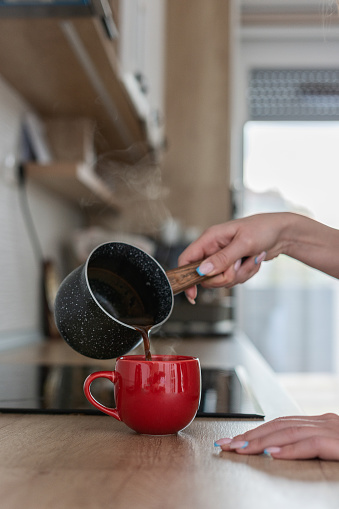 Unrecognizable woman pouring morning coffee in coffee cup in the kitchen