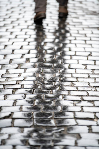 un homme marchant sur une route pavée, par une pluie. - paving stone cobblestone road old photos et images de collection