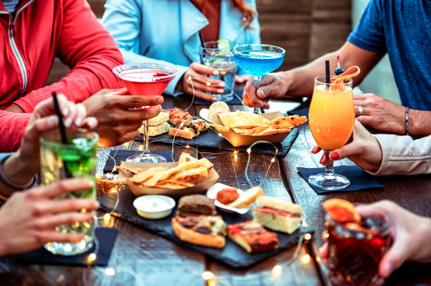 grupo de amigos disfrutando de un aperitivo bebiendo y comiendo en un bar - primer plano de manos de jóvenes sosteniendo coloridos cócteles en la hora feliz - concepto de tiempo de fiesta de reunión social - hora feliz fotografías e imágenes de stock