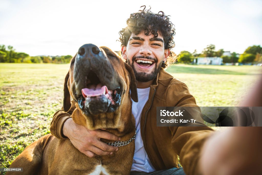 Young Happy Man Taking Selfie With His Dog In A Park Smiling Guy And Puppy Having Fun Together Outdoor Friendship And Love Between Humans And Animals Concept Stock Photo - Download Image Young Happy Man Taking Selfie With His Dog In A Park Smiling Guy And Puppy Having Fun Together Outdoor Friendship And Love Between Humans And Animals Concept Stock Photo - Download Image
