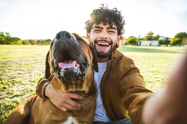 Young happy man taking selfie with his dog in a park - Smiling guy and puppy having fun together outdoor - Friendship and love between humans and animals concept stock photo