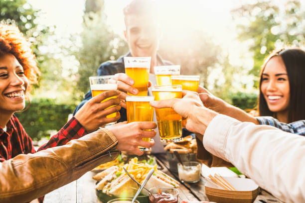 醸造所のバーレストランでビールを飲んで幸せな時間を祝う幸せな友人 - 裏庭のディナーパーティーで楽しんでいるマルチエスニックファミリー - オープンエアのパブで一緒に時間を楽しむ� - beer ストックフォトと画像