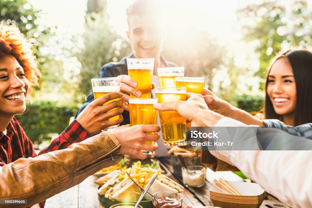 Happy friends celebrating happy hour drinking beer at brewery bar restaurant - Multi ethnic family having fun at backyard dinner party - Young people enjoying time together at open air pub Beer - Alcohol Stock Photo