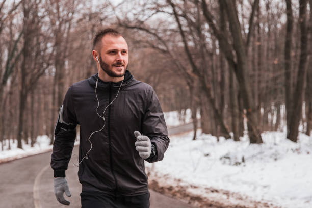 istock Man wearing jacket and gloves jogging while listening music 1350404907