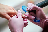 Woman uses electric nail file drill in beauty salon. Close up of nail manicure process.