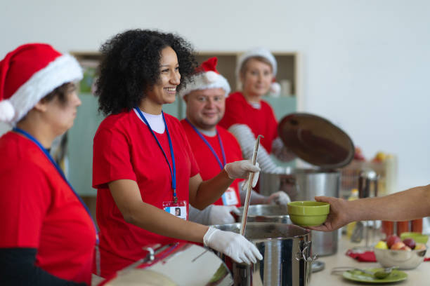 A hand holding a bowl to receive a portion of soup from a smiling volunteer stock photo