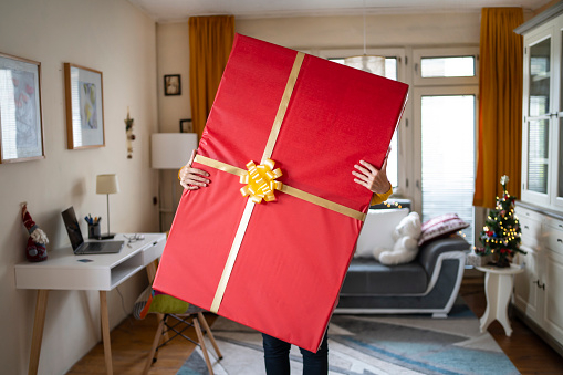 Holding with both hands a very large Christmas gift at home