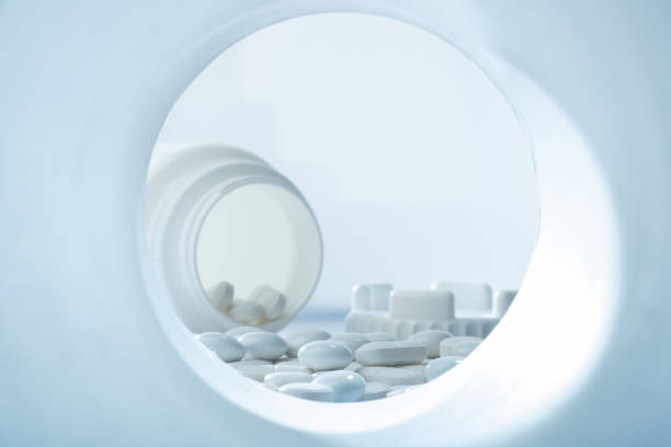 Closeup of white pills against white background with plastic pill container in the background with plastic pill container stock photo