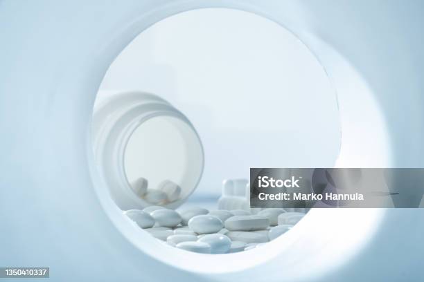 Closeup Of White Pills Against White Background With Plastic Pill Container In The Background With Plastic Pill Container Stock Photo - Download Image Now