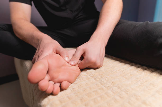 足のセルフマッサージをしている白人の若者をクローズアップ。プロのマッサージ師は足の表面のマッサージの正しい実装を示す - reflexology massaging recovery sport ストックフォトと画像