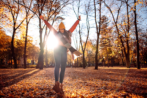 Carefree young woman having fun in an autumn park flinging her legs and arms in the air