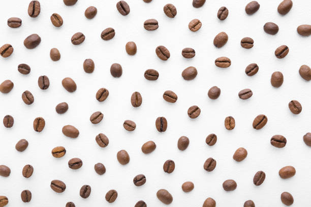 白いテーブルの上に新鮮なダークブラウンのコーヒー豆。パターンの背景。クローズ アップ。トップダウンビュー。 - coffee crop bean seed directly above ストックフォトと画像