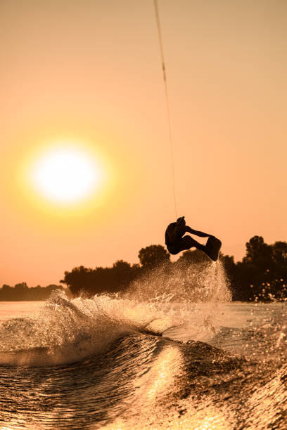 istock active man making trick with wakeboard on bright orange sky and sun background. 1350417322