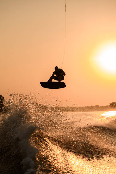 istock silhouette of active man making trick with wakeboard on bright orange sky and sun background. 1350417349