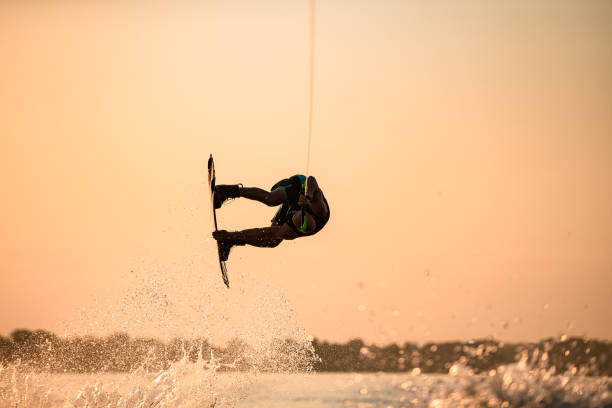 istock man skillfully making trick in jump with wakeboard on bright orange sky and sun background. 1350418435