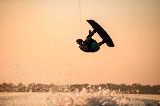 istock man making trick in jump with wakeboard on bright orange sky and sun background. 1350418452