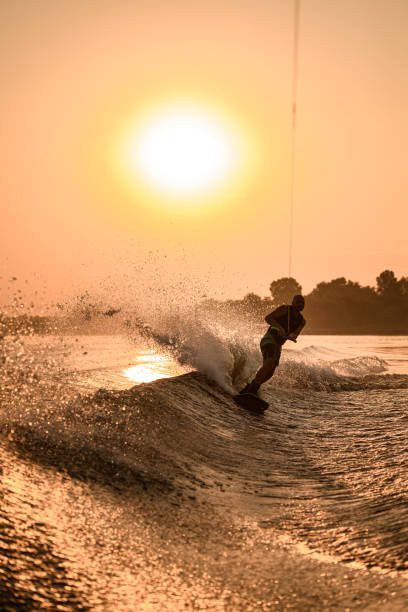 istock active man ride down the wave on wakeboard on bright orange sky and sun background. 1350418693