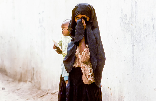 Hadramaut, Yemen - July 4, 1991: arabic unknown mother carries her baby in a  wraparound garment in Hadramaut, Yemen. She wears a burqa in black but don`t wears a niqab who covers the face.