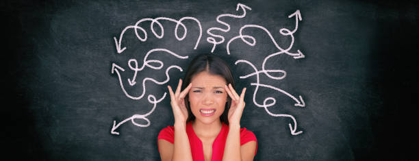Confused woman confusion illustrated on blackboard with chalk drawing of arrows going everywhere around head showing indecision. Indecisive stressed Asian girl with headache panoramic banner. stock photo