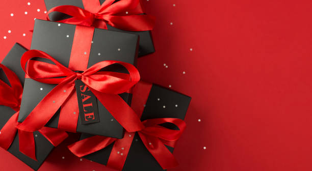 istock Top panoramic view photo of sequins stack of black gift boxes with red ribbon bow and tag on isolated red background with copyspace 1350429738