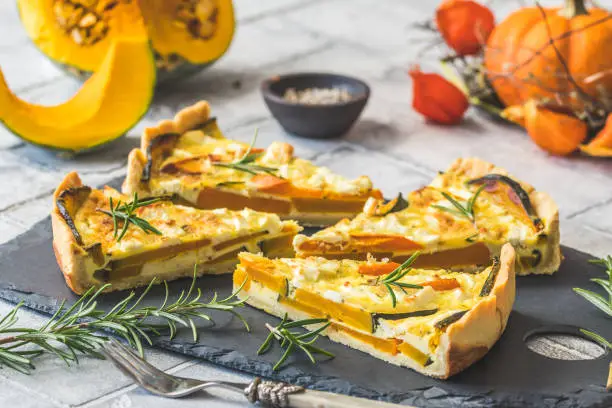 Pieces of pumpkin tart with rosemary on a slate plate on gray background