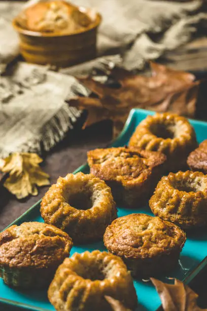 Homemade delicious mini bundt cakes, guglhupf, muffins on a blue plate on rustic wooden background with autumn decoration, vertical