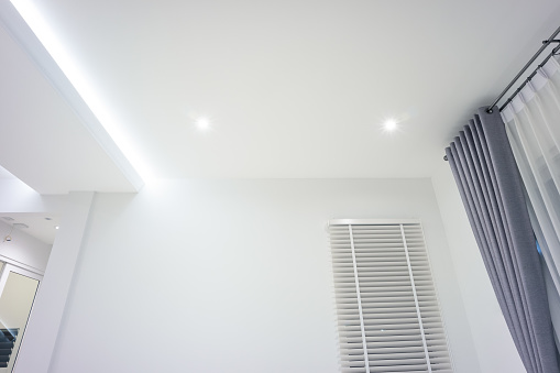 LED strip light and illumination. Also called ribbon light or LED tape. That suspended on ceiling and hide in plasterboard in empty living room include down light, white wall, window, air conditioner, adjusting vertical or venetian blinds, eyelet curtains both blackout and translucent. That is modern luxury interior home building design and technology.