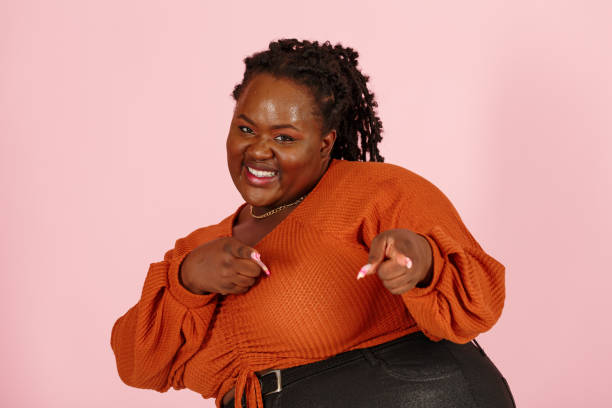 istock Cheerful young black plus size woman points to camera with fingers on pink 1350433504