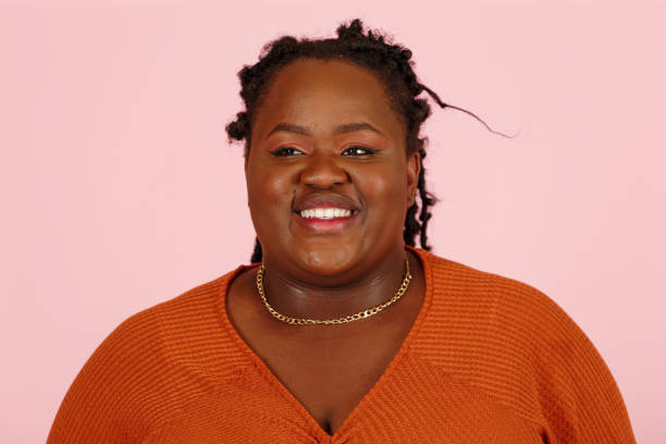 Shy black woman smiles to camera on pink background stock photo