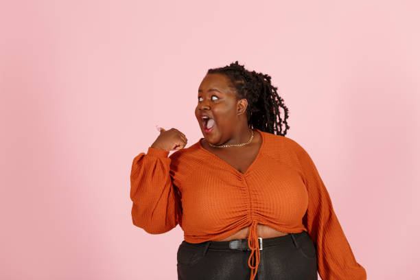 istock Funny black body positive woman points aside on pink background 1350433729