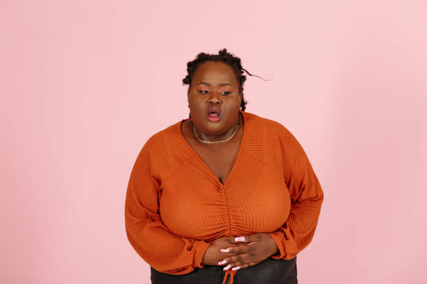 Young black plus size woman patient suffers from stomach ache on light pink background stock photo