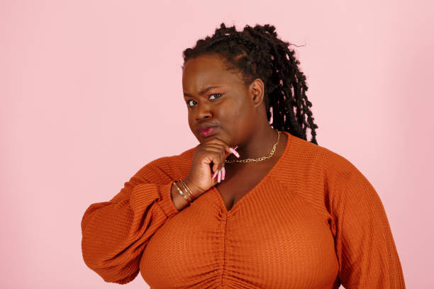 istock Skeptical black plus size woman touches chin on pink background 1350434444