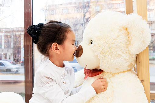 girl child hugs a big teddy bear toy and looks at it.