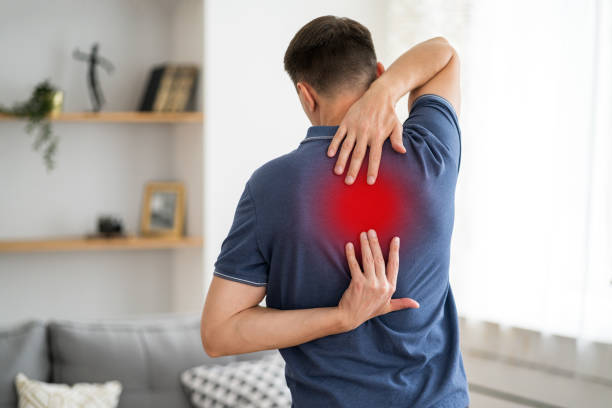 Pain between the shoulder blades, man suffering from backache at home, painful area highlighted in red