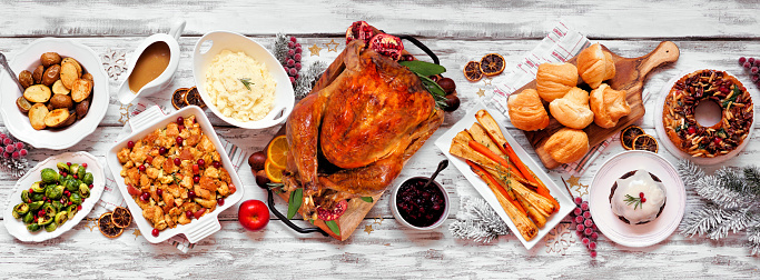 Traditional Christmas turkey dinner. Overhead view table scene on a white wood banner background. Turkey, potatoes and sides, dressing, fruit cake and plum pudding.