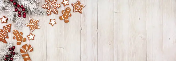 Photo of Christmas corner border of gingerbread cookies and frosty tree branches. Above view on a grey wood banner background.