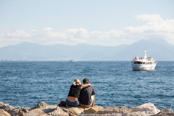 Naples, Italy, October 2021: Young couple enjoying the afternoon sun at the port of Mergellina with view of the Gulf of Naples.